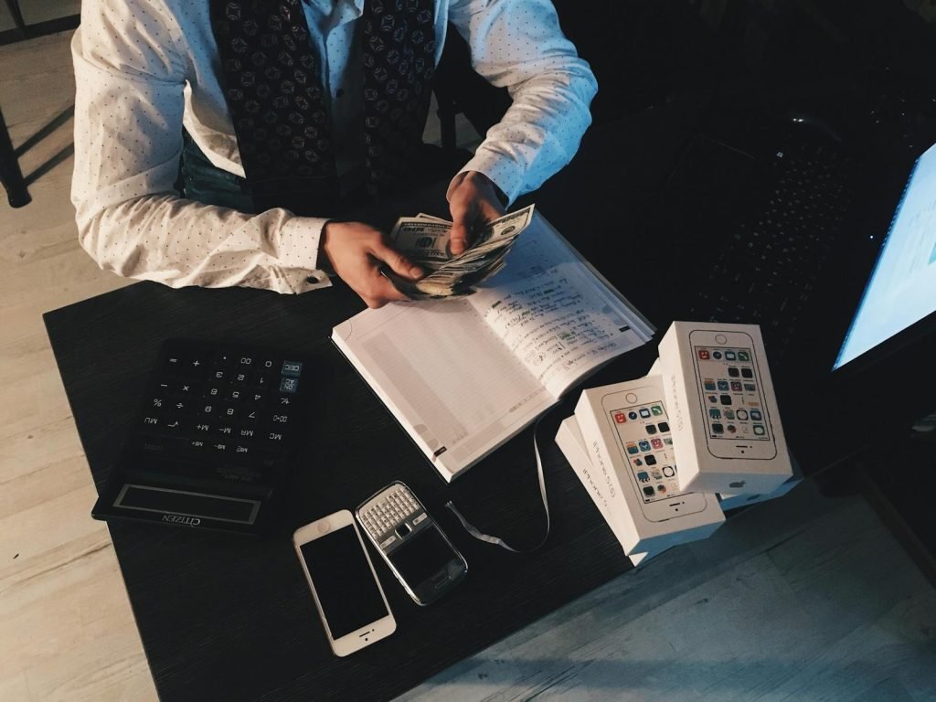 A person counting banknotes at a desk beside a calculator and a notebook