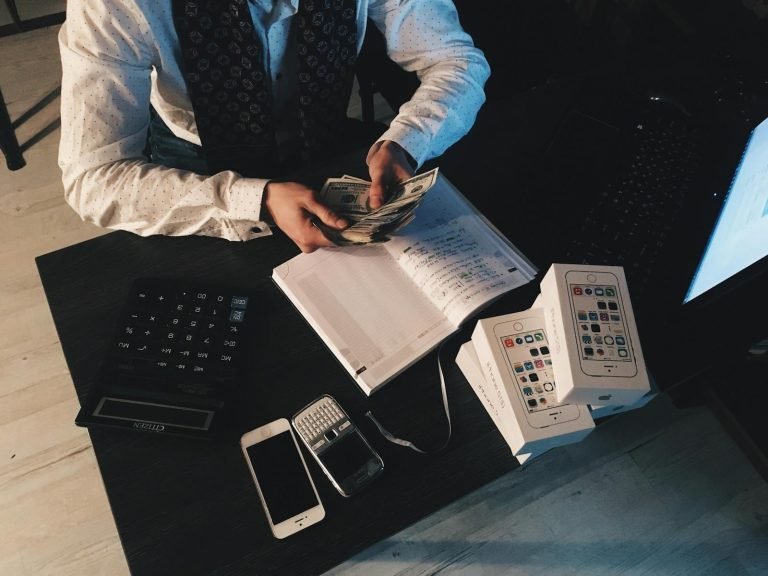 A person counting banknotes at a desk beside a calculator and a notebook